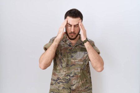 Photo for Young hispanic man wearing camouflage army uniform with hand on head for pain in head because stress. suffering migraine. - Royalty Free Image