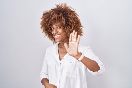 Photo for Young hispanic woman with curly hair standing over white background waiving saying hello happy and smiling, friendly welcome gesture - Royalty Free Image