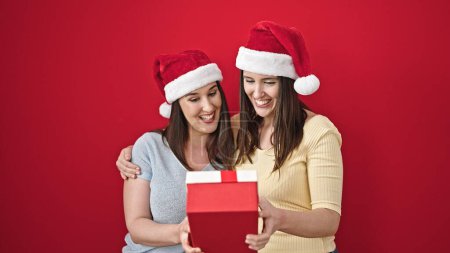 Foto de Dos mujeres sorprendentes con regalo de Navidad sobre fondo rojo aislado - Imagen libre de derechos