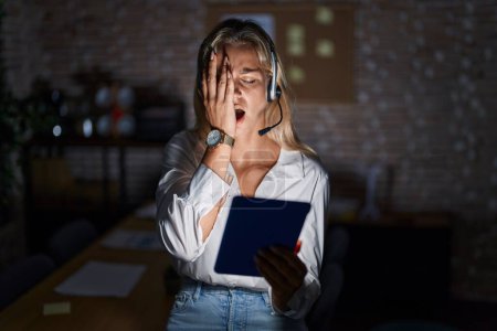 Photo for Young blonde woman working at the office at night yawning tired covering half face, eye and mouth with hand. face hurts in pain. - Royalty Free Image