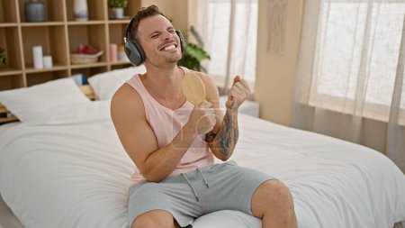 Foto de Feliz hombre tatuado disfrutando de la música con auriculares en un dormitorio luminoso - Imagen libre de derechos