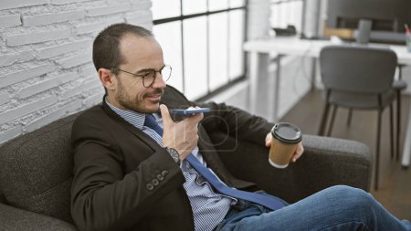 A confident man speaks on a smartphone in his modern office, displaying professionalism and technology in a relaxed pose.