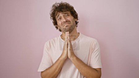 Photo for A pensive young man with curly hair praying or wishing against a pink wall, evoking hope or desire. - Royalty Free Image