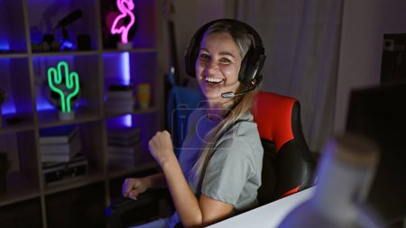 Foto de Una joven alegre con un auricular celebra mientras juega por la noche en una habitación iluminada por neón. - Imagen libre de derechos