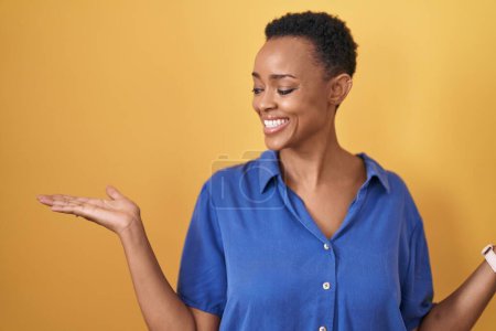 Téléchargez les photos : Femme afro-américaine debout sur fond jaune souriant montrant les paumes ouvertes des deux mains, présentant et comparant la publicité et l'équilibre - en image libre de droit