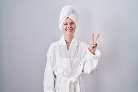 Téléchargez les photos : Blonde femme caucasienne portant peignoir montrant et pointant vers le haut avec les doigts numéro deux tout en souriant confiant et heureux. - en image libre de droit