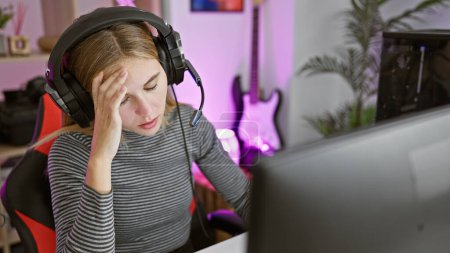 Foto de Mujer estresada con auriculares en una sala de juegos por la noche mirando la pantalla de una computadora. - Imagen libre de derechos