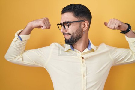 Téléchargez les photos : Jeune homme hispanique portant des vêtements de travail et des lunettes montrant les muscles des bras souriant fier. concept de fitness. - en image libre de droit