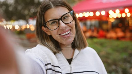 Foto de Mujer joven sonriente con gafas en un café al aire libre durante la noche - Imagen libre de derechos