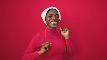 Foto de Mujer afroamericana con sombrero de navidad bailando sobre fondo rojo aislado - Imagen libre de derechos