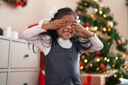 Foto de Adorable chica hispana de pie junto al árbol de Navidad con los ojos cerrados en casa - Imagen libre de derechos