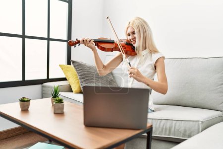 Téléchargez les photos : Jeune femme blonde musicienne souriante confiante ayant une leçon de violon en ligne à la maison - en image libre de droit