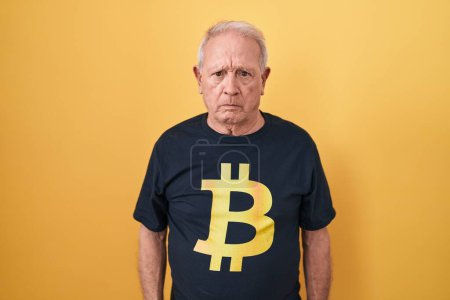 Foto de Hombre mayor con el pelo gris usando camiseta Bitcoin escéptico y nervioso, frunciendo el ceño molesto debido a un problema. persona negativa. - Imagen libre de derechos
