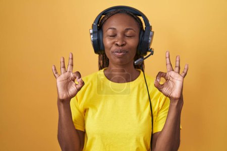 Photo for African american woman listening to music using headphones relax and smiling with eyes closed doing meditation gesture with fingers. yoga concept. - Royalty Free Image