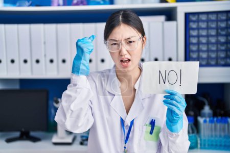 Téléchargez les photos : Jeune femme chinoise travaillant au laboratoire scientifique ne tenant aucune bannière ennuyée et frustrée criant de colère, criant fou de colère et la main levée - en image libre de droit