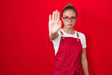Photo for Young hispanic woman wearing waitress apron over red background doing stop sing with palm of the hand. warning expression with negative and serious gesture on the face. - Royalty Free Image