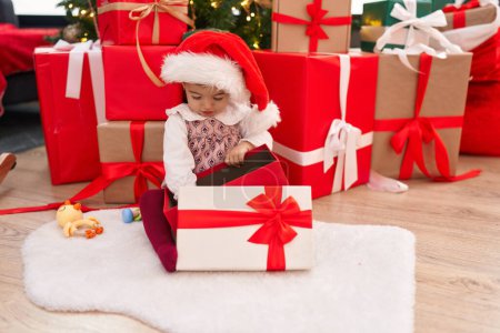 Foto de Adorable rubia niño desempacar regalo sentado junto al árbol de Navidad en casa - Imagen libre de derechos