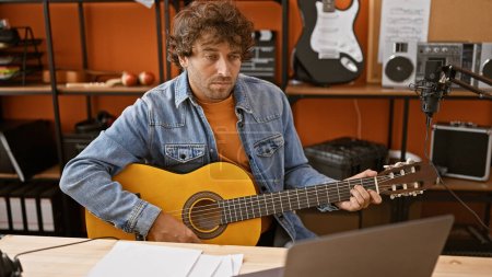 Téléchargez les photos : Homme concentré jouant de la guitare dans un studio de musique maison avec un équipement d'enregistrement et un microphone. - en image libre de droit