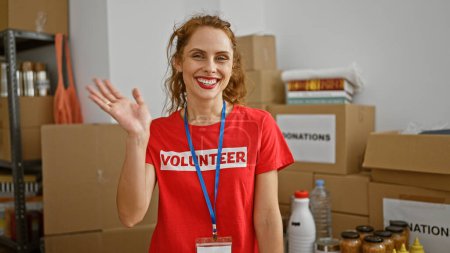 Photo for Smiling caucasian woman volunteer waving in warehouse full of donations. - Royalty Free Image
