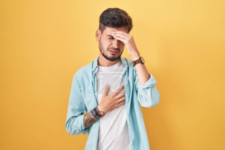 Téléchargez les photos : Young hispanic man with tattoos standing over yellow background touching forehead for illness and fever, flu and cold, virus sick - en image libre de droit