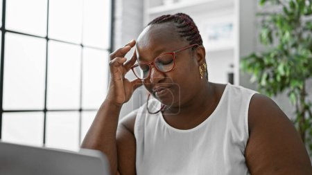 Foto de Mujer afroamericana estresada trabajando en la computadora portátil, luchando contra el estrés empresarial en la oficina desgarradoramente - Imagen libre de derechos