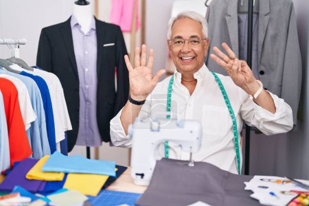 Photo for Middle age man with grey hair dressmaker using sewing machine showing and pointing up with fingers number eight while smiling confident and happy. - Royalty Free Image