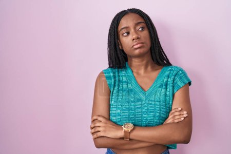 Téléchargez les photos : Jeune afro-américain avec des tresses debout sur fond rose regardant sur le côté avec les bras croisés convaincu et confiant - en image libre de droit