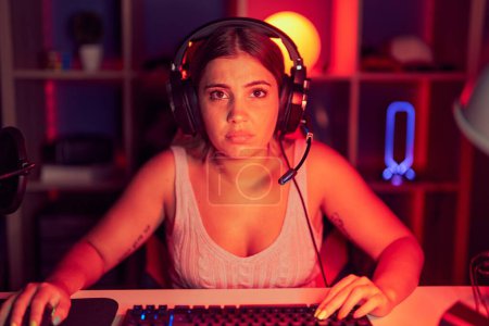 Téléchargez les photos : Jeune femme blonde jouant à des jeux vidéo portant des écouteurs déprimés et inquiets pour la détresse, pleurant en colère et effrayés. triste expression. - en image libre de droit