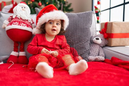 Téléchargez les photos : Adorable fille hispanique assise sur le canapé près de l'arbre de Noël à la maison - en image libre de droit