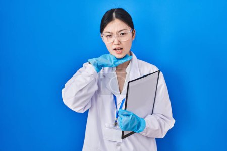 Téléchargez les photos : Une jeune femme chinoise travaillant au laboratoire scientifique tranchant la gorge avec la main comme un couteau, menace d'agression avec une violence furieuse - en image libre de droit