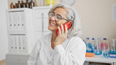 Foto de Científica sonriente hablando en un smartphone rojo en un entorno de laboratorio, mostrando profesionalidad y comunicación - Imagen libre de derechos