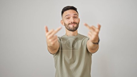 Foto de Joven hombre hispano sonriendo confiado haciendo gesto del dedo medio sobre fondo blanco aislado - Imagen libre de derechos