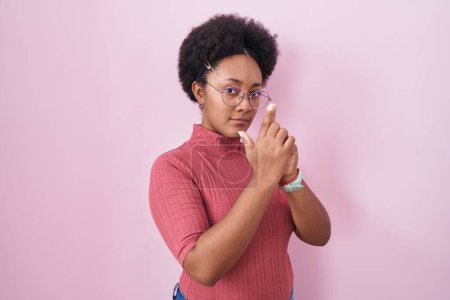Photo for Beautiful african woman with curly hair standing over pink background holding symbolic gun with hand gesture, playing killing shooting weapons, angry face - Royalty Free Image