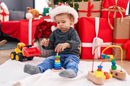 Téléchargez les photos : Adorable bambin blond jouant avec des jouets assis sur le sol par des cadeaux de Noël à la maison - en image libre de droit