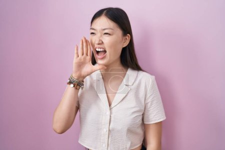 Téléchargez les photos : Jeune femme chinoise debout sur fond rose criant et criant fort à côté avec la main sur la bouche. concept de communication. - en image libre de droit