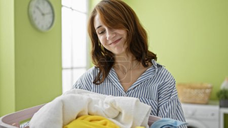 Photo for Young woman smiling confident holding basket with clothes at laundry room - Royalty Free Image