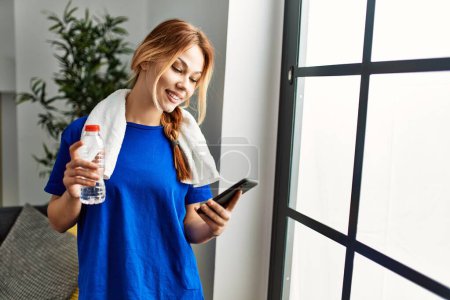 Téléchargez les photos : Young caucasian woman smiling confident holding water using smartphone at home - en image libre de droit