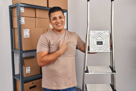 Téléchargez les photos : Jeune homme hispanique travaillant dans une petite entreprise e-commerce tenant échelles souriant heureux pointant avec la main et le doigt - en image libre de droit