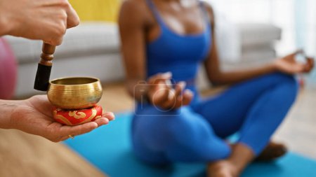 Téléchargez les photos : Femme afro-américaine formation yoga en utilisant bol de chant tibétain à la maison - en image libre de droit