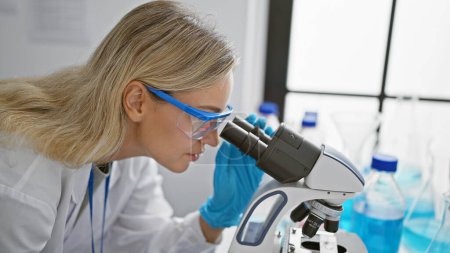 Foto de Científica rubia usando microscopio en laboratorio, retratando investigación médica en interiores. - Imagen libre de derechos