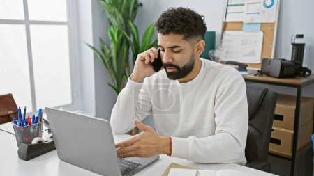 Téléchargez les photos : Bel homme hispanique avec barbe parler au téléphone dans le bureau moderne - en image libre de droit