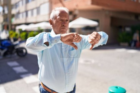 Foto de Hombre de pelo gris de mediana edad haciendo signo negativo con pulgares en la calle - Imagen libre de derechos