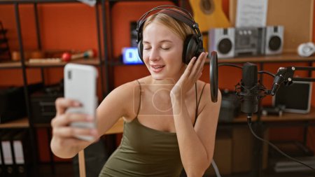 Téléchargez les photos : Jeune femme blonde musicienne ayant un appel vidéo souriant au studio de podcast - en image libre de droit