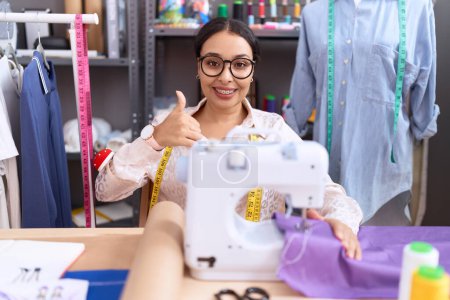 Photo for Young arab woman dressmaker designer working at atelier doing happy thumbs up gesture with hand. approving expression looking at the camera showing success. - Royalty Free Image