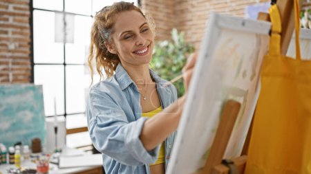 Photo for Smiling caucasian woman artist painting on canvas in a bright studio - Royalty Free Image