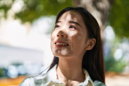 Téléchargez les photos : Jeune femme chinoise souriant confiant regardant vers le ciel au parc - en image libre de droit
