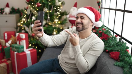 Photo for Young hispanic man having video call singing song by christmas tree at home - Royalty Free Image
