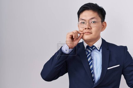 Foto de Joven hombre asiático con traje de negocios y corbata boca y labios cerrados como cremallera con los dedos. secreto y silencioso, tabú hablando - Imagen libre de derechos