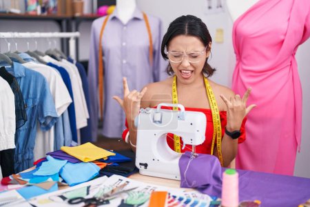 Photo for Hispanic young woman dressmaker designer using sewing machine shouting with crazy expression doing rock symbol with hands up. music star. heavy music concept. - Royalty Free Image