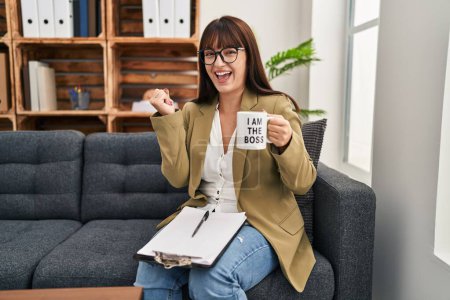 Photo for Young hispanic woman drinking from i am the boss coffee cup screaming proud, celebrating victory and success very excited with raised arm - Royalty Free Image